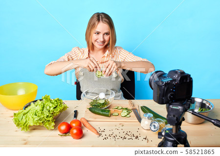 Female chef sits at table with products, makes healthy salad with vegetables 58521865