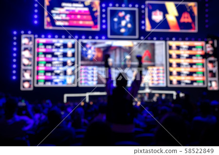 Blurred background of an esports event - Fan on a tribune at tournament's arena with hands raised. Blurred background of an esports event - Fan on a tribune at tournament's arena with hands raised. 58522849