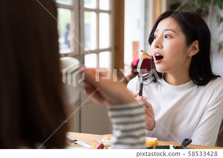 年輕女子在咖啡館裡聊天，一邊拿著煎餅用叉子刺傷 58533428