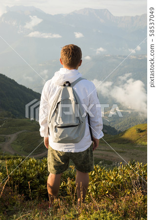 Male tourist with a backpack on his back stands and looks at the mountains. Male tourist with a backpack on his back stands and looks at the mountains. 58537049