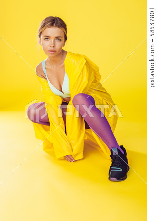 Young woman in a yellow raincoat, purple tights and sneakers. 58537801