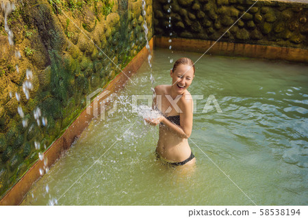 Young woman in hot springs banjar. Thermal water is released from the mouth of statues at a hot Young woman in hot springs banjar. Thermal water is released from the mouth of statues at a hot 58538194