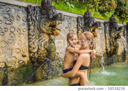 Mom and son travelers in hot springs banjar. Thermal water is released from the mouth of statues at Mom and son travelers in hot springs banjar. Thermal water is released from the mouth of statues at 58538238