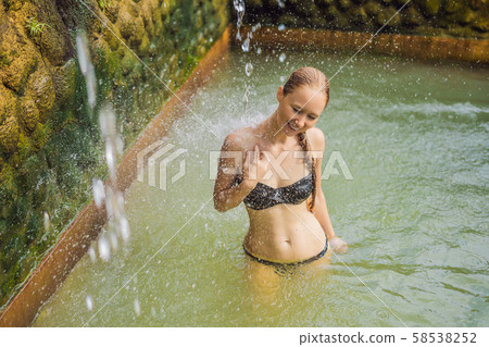 Young woman in hot springs banjar. Thermal water is released from the mouth of statues at a hot Young woman in hot springs banjar. Thermal water is released from the mouth of statues at a hot 58538252