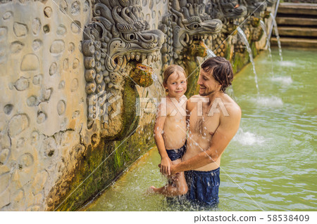 Dad and son travelers in hot springs banjar. Thermal water is released from the mouth of statues at Dad and son travelers in hot springs banjar. Thermal water is released from the mouth of statues at 58538409