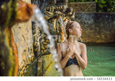 Young woman in hot springs banjar. Thermal water is released from the mouth of statues at a hot Young woman in hot springs banjar. Thermal water is released from the mouth of statues at a hot 58538413