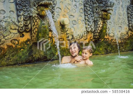 Dad and son travelers in hot springs banjar. Thermal water is released from the mouth of statues at Dad and son travelers in hot springs banjar. Thermal water is released from the mouth of statues at 58538416