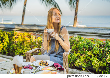 Young woman having romantic breakfast in sunrise at resort restaurant outdoor. Healthy food drink Young woman having romantic breakfast in sunrise at resort restaurant outdoor. Healthy food drink 58538417