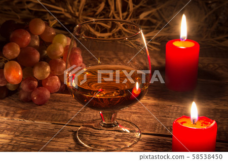 glass with brandy or cognac, grapes and candle on aged wood table background. Close-up view. 58538450