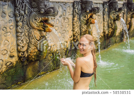 Young woman in hot springs banjar. Thermal water is released from the mouth of statues at a hot Young woman in hot springs banjar. Thermal water is released from the mouth of statues at a hot 58538531