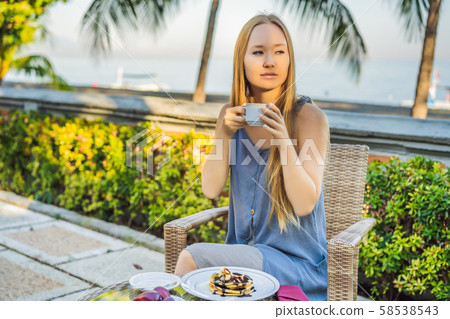Young woman having romantic breakfast in sunrise at resort restaurant outdoor. Healthy food drink Young woman having romantic breakfast in sunrise at resort restaurant outdoor. Healthy food drink 58538543