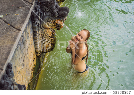 Young woman in hot springs banjar. Thermal water is released from the mouth of statues at a hot Young woman in hot springs banjar. Thermal water is released from the mouth of statues at a hot 58538597