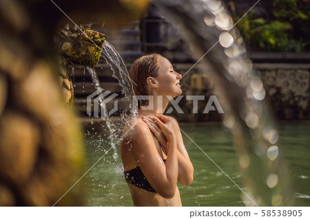 Young woman in hot springs banjar. Thermal water is released from the mouth of statues at a hot Young woman in hot springs banjar. Thermal water is released from the mouth of statues at a hot 58538905