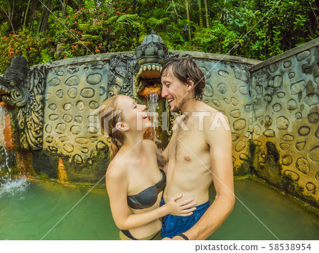 Young man and woman in hot springs banjar. Thermal water is released from the mouth of statues at a Young man and woman in hot springs banjar. Thermal water is released from the mouth of statues at a 58538954