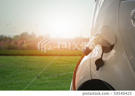 Close up of electric car with a connected charging cable on the blurred background of a city using renewable energy Close up of electric car with a connected charging cable on the blurred background of a city using renewable energy 58540425