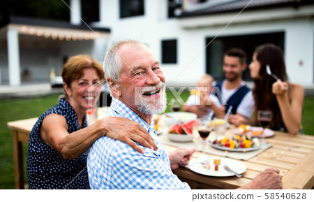 Portrait of multigeneration family sitting at table outdoors on garden barbecue. 58540628