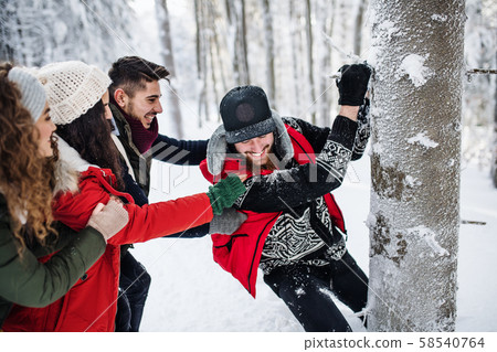 A group of young friends on a walk outdoors in snow in winter forest. 58540764
