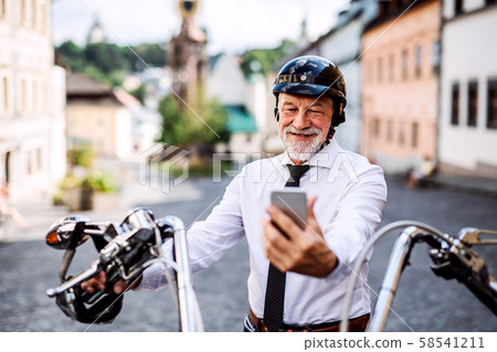 A senior businessman with motorbike in town, using smartphone. A senior businessman with motorbike in town, using smartphone. 58541211