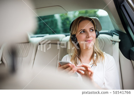 Business woman with smartphone and headphones sitting on back seats in taxi car. Business woman with smartphone and headphones sitting on back seats in taxi car. 58541766