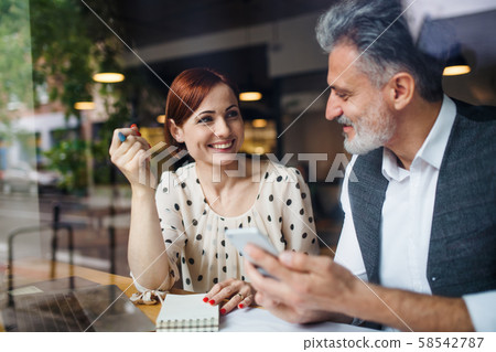 Man and woman having business meeting in a cafe, using smartphone. Man and woman having business meeting in a cafe, using smartphone. 58542787