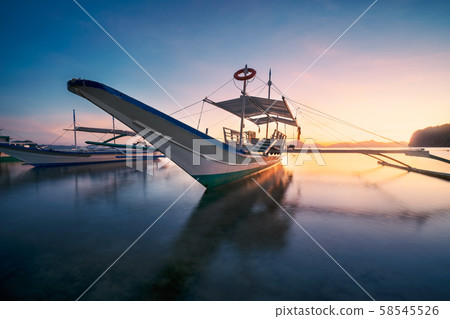El Nido, Palawan, Philippines. Traditional banca boat in the beach bay in golden sunset light El Nido, Palawan, Philippines. Traditional banca boat in the beach bay in golden sunset light 58545526