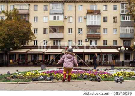 Toddler girl in rain boots playing with birds on city square. Outdoors childhood activity Toddler girl in rain boots playing with birds on city square. Outdoors childhood activity 58546029
