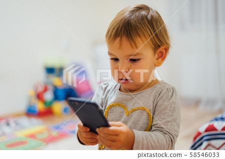 Baby using phone, playing game or watching cartoons. Home indoors. Screen time Baby using phone, playing game or watching cartoons. Home indoors. Screen time 58546033
