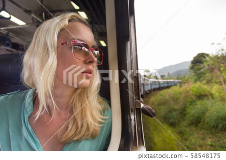 Happy smiling woman looks out from window traveling by train on most picturesque train road in Sri 58548175