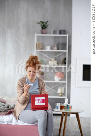Red-haired woman taking thermometer out of first aid kit 58555217