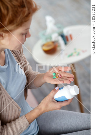 Sick woman suffering from flu holding pills on palm Sick woman suffering from flu holding pills on palm 58555231