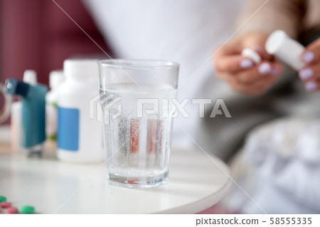 Close up of pill dissolving in glass of water standing on table Close up of pill dissolving in glass of water standing on table 58555335