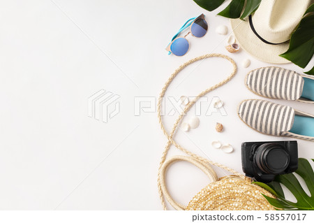 Straw hat, camera, bag, summer shoes, sunglasses, shells and tropical leaves over white background 58557017
