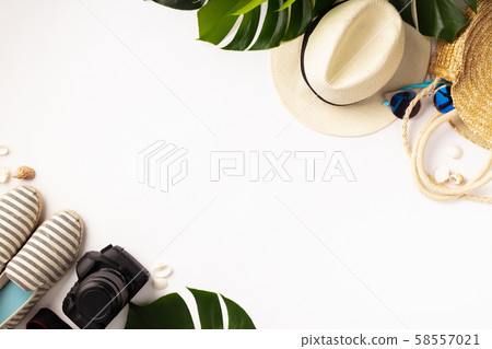 Straw hat, camera, bag, summer shoes, sunglasses, shells and tropical leaves over white background 58557021