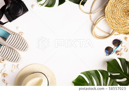 Straw hat, camera, bag, summer shoes, sunglasses, shells and tropical leaves over white background 58557023