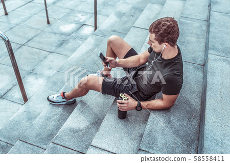 Athletic man resting in summer on steps city. Rest after workout with fitness and outdoor workout 58558411