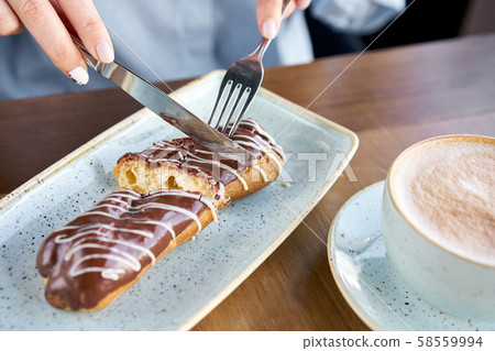 A young woman drinks coffee cappuccino in a restaurant and eats dessert. Traditional french eclairs A young woman drinks coffee cappuccino in a restaurant and eats dessert. Traditional french eclairs 58559994