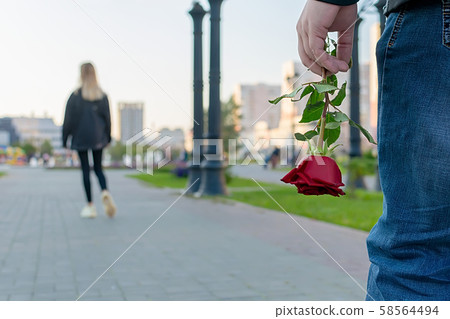 red rose flower in the hand of the guy on the background of the girl leaving him red rose flower in the hand of the guy on the background of the girl leaving him 58564494