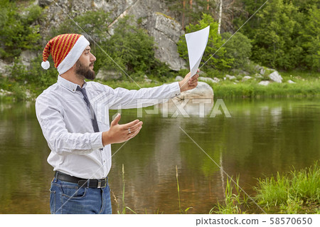 Young man with a beard in a Santa Claus hat with a Young man with a beard in a Santa Claus hat with a 58570650