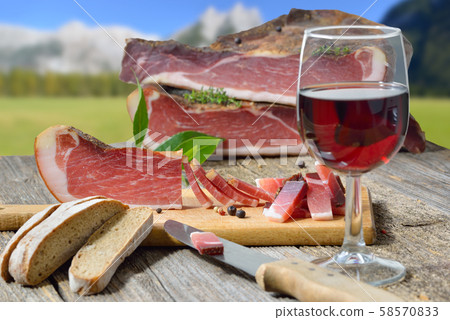 Typical South Tyrolean bacon snack with rye bread lying in front of alpine pastures of the alps 58570833