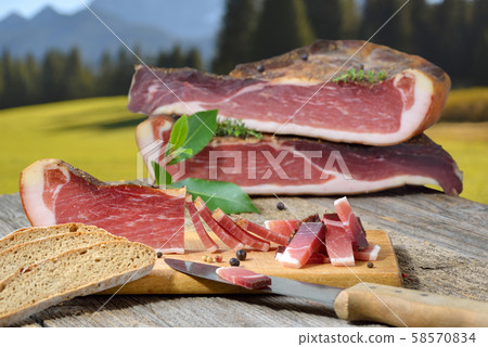 Typical South Tyrolean bacon snack with rye bread lying in front of alpine pastures of the alps Typical South Tyrolean bacon snack with rye bread lying in front of alpine pastures of the alps 58570834