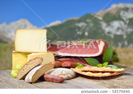 South Tyrolean specialties like bacon, sausages and cheese lying in front of mountains of the alps 58570840