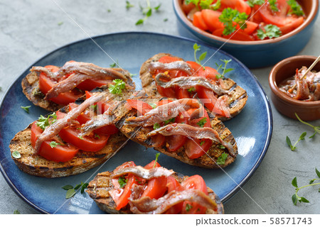 Spanish bar food: Grilled slices of bread with olive oil, herbs, fresh tomatoes and anchovy fillets Spanish bar food: Grilled slices of bread with olive oil, herbs, fresh tomatoes and anchovy fillets 58571743