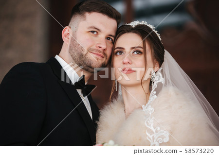 Young bride with groom stand on balcony. Bride in fur coat in winter time Young bride with groom stand on balcony. Bride in fur coat in winter time 58573220