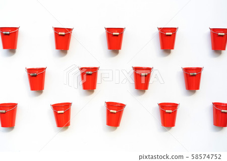 Several red buckets with a wooden handle hang nailed on a white wall 58574752