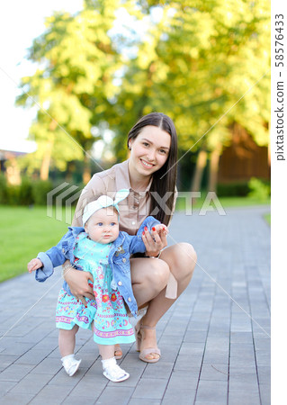 Young brunette woman walking with little daughter in park. 58576433