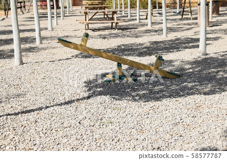 Wooden seesaw in a public park on a summer afternoon surrounded by trees 58577787