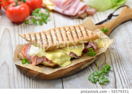 Grilled and pressed toast with smoked ham, cheese, tomato and lettuce served on a wooden table 58579351