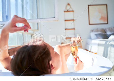 Photo from back of woman with wine glass with wine in her hands lying in bath. Photo from back of woman with wine glass with wine in her hands lying in bath. 58579632