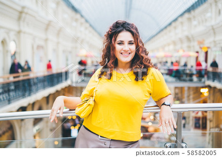 Beautiful cheerful curly woman in a bright yellow sweater with a handbag Beautiful cheerful curly woman in a bright yellow sweater with a handbag 58582005