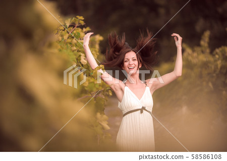Smiling woman in white dress standing in vineyard Smiling woman in white dress standing in vineyard 58586108